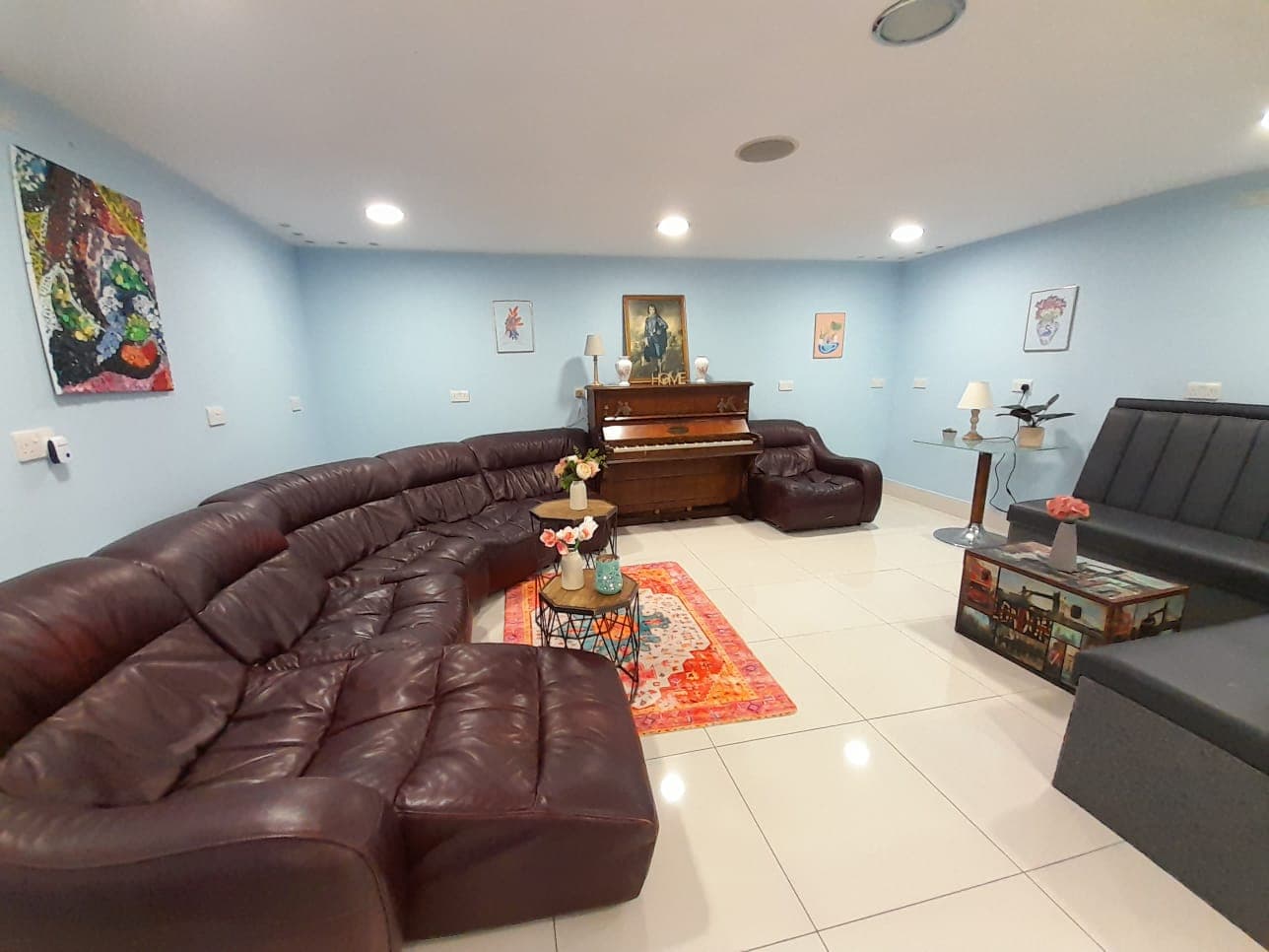 Large curved brown leather sofa and upright piano in a spacious, light blue living room.